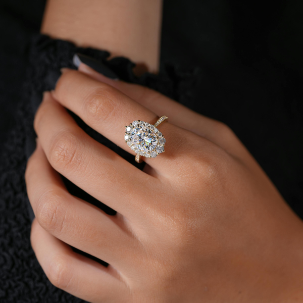 An oval halo engagement ring in yellow gold, worn on the hand