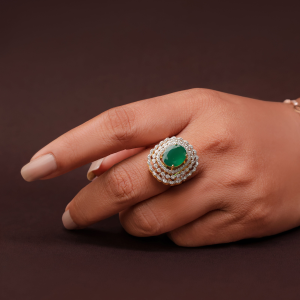 An oval emerald ring with layered diamond halos in yellow gold, worn on the hand
